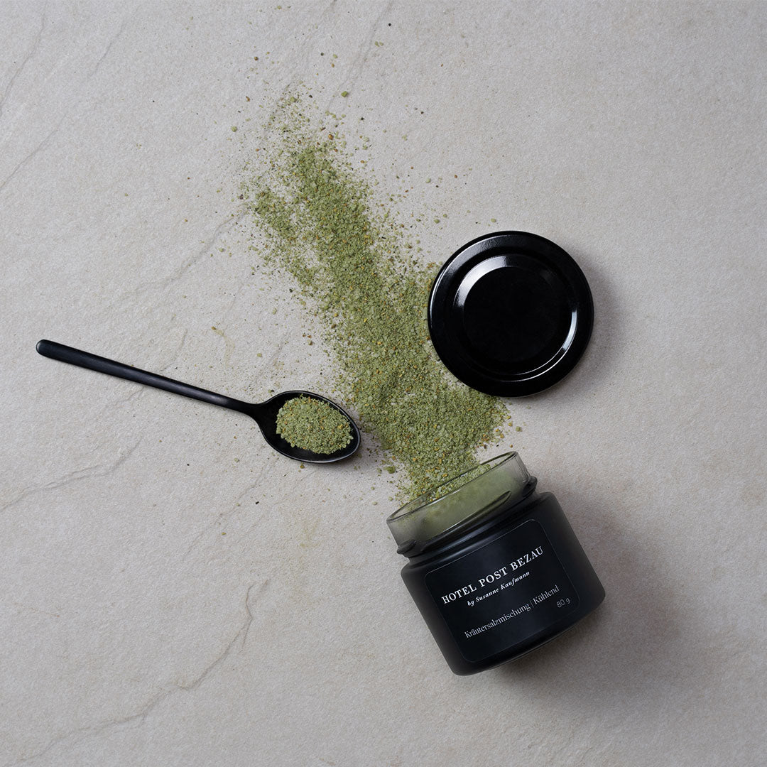 Hotel Post Bezau Kräutersalzmischung Kühlend auf dem Tisch verstreut aus dem geöffneten Glas mit Deckel und Kräutersalzmischung auf einem Löffel