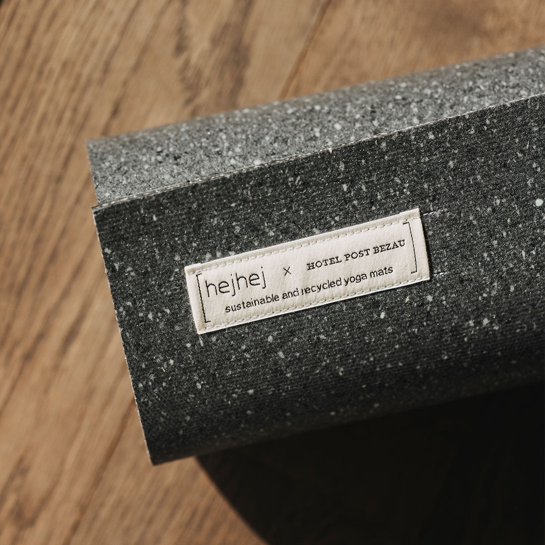 Eher dunkle Yogamatte von hejhej-mats und Hotel Post Bezau, zusammengerollt mit Logo
